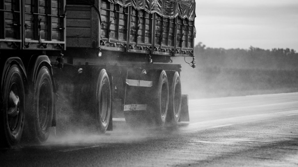 Rain or Shine: Delivering On Time Across Vancouver Black and white image of a truck driving on a rain-soaked road.